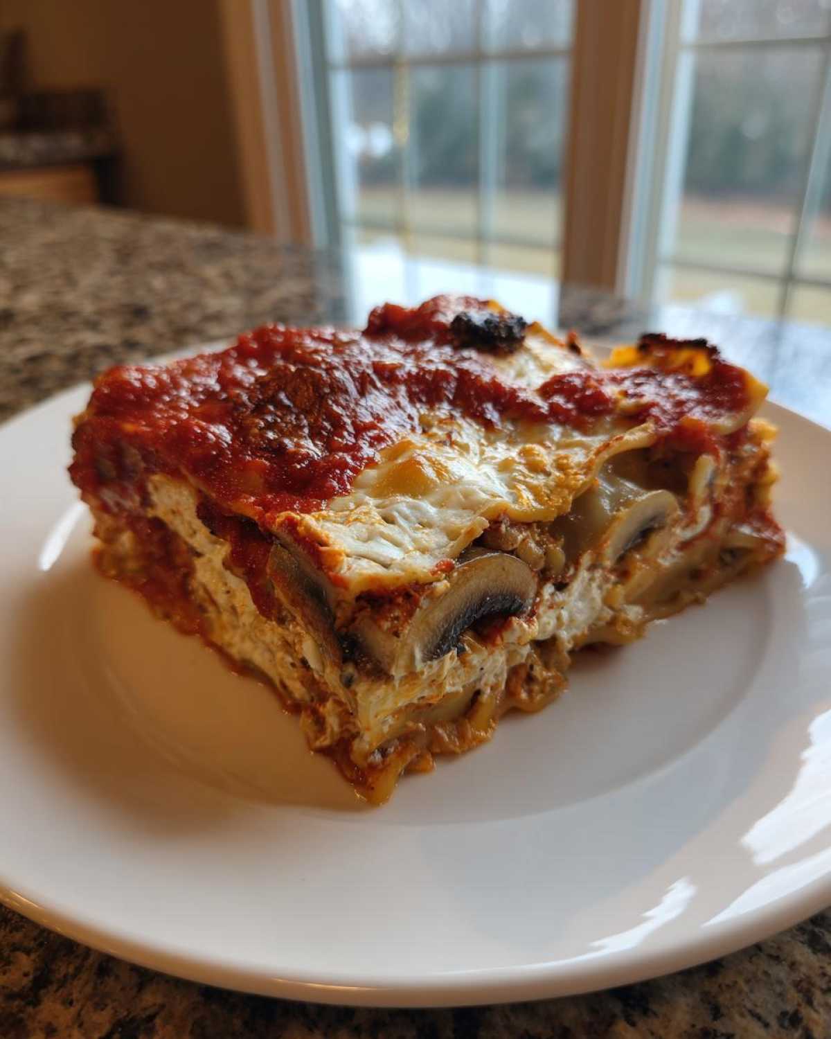 A generous slice of Vegan Dumpling Lasagna featuring layers of pasta, creamy filling, mushrooms, and topped with rich tomato sauce.