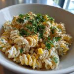 Close-up of a serving of Vegan Elote Pasta Salad featuring fusilli pasta coated in a creamy sauce, topped with corn, chili powder, and fresh parsley.