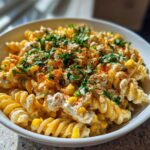 Close-up of a white bowl filled with Vegan Elote Pasta Salad, featuring fusilli pasta, creamy sauce, corn, and topped with chili powder and cilantro.