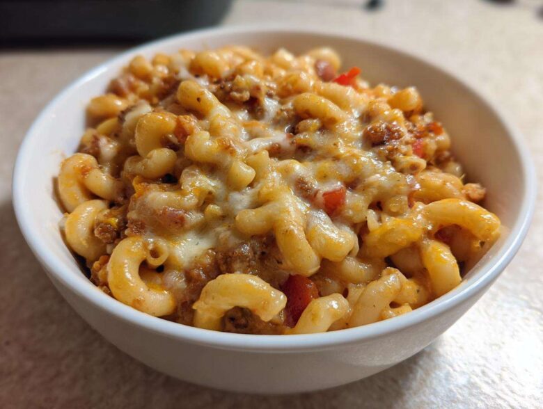 Close-up of a white bowl filled with cheesy Vegetarian Chili Mac, featuring elbow macaroni and melted cheese topping.