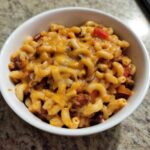 Close-up of a white bowl filled with Vegetarian Chili Mac topped with melted cheddar cheese.