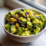 Close-up of a bright Avocado Salad featuring diced avocado, black beans, and yellow corn kernels in a white bowl.