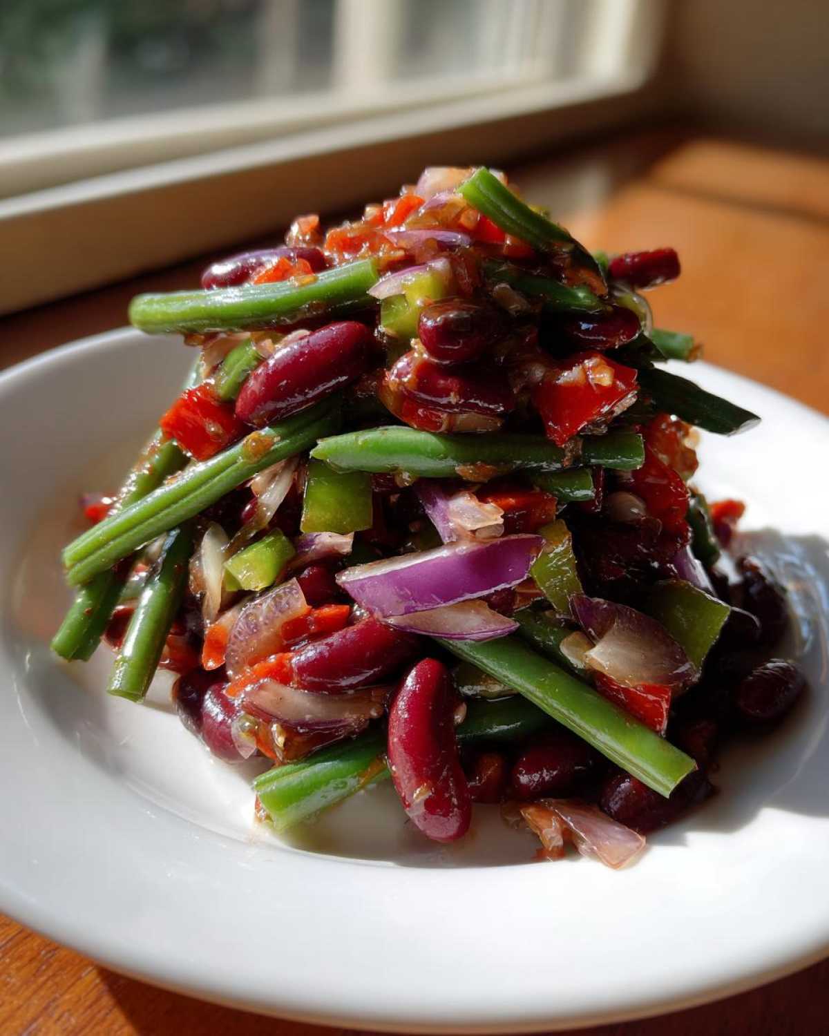 A close-up of a vibrant Bean Salad featuring kidney beans, green beans, red onion, and peppers tossed in a dressing.