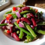 Close-up of a vibrant Bean Salad featuring kidney beans, green beans, red onion, and red peppers on a white plate.