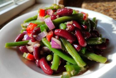 Close-up of a vibrant Bean Salad featuring kidney beans, green beans, red onion, and red peppers on a white plate.